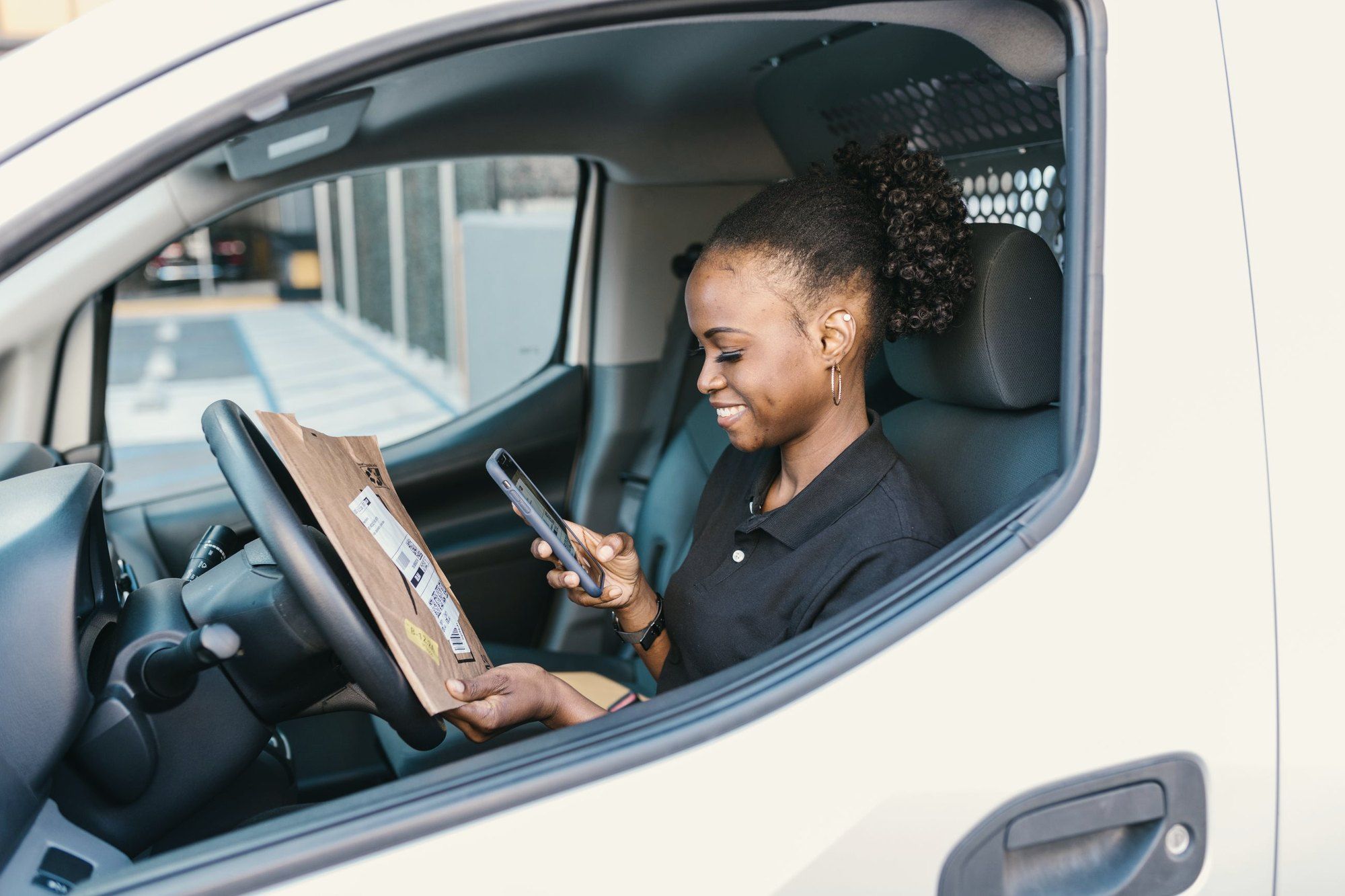 Entregadora confere o pedido no celular de dentro do carro